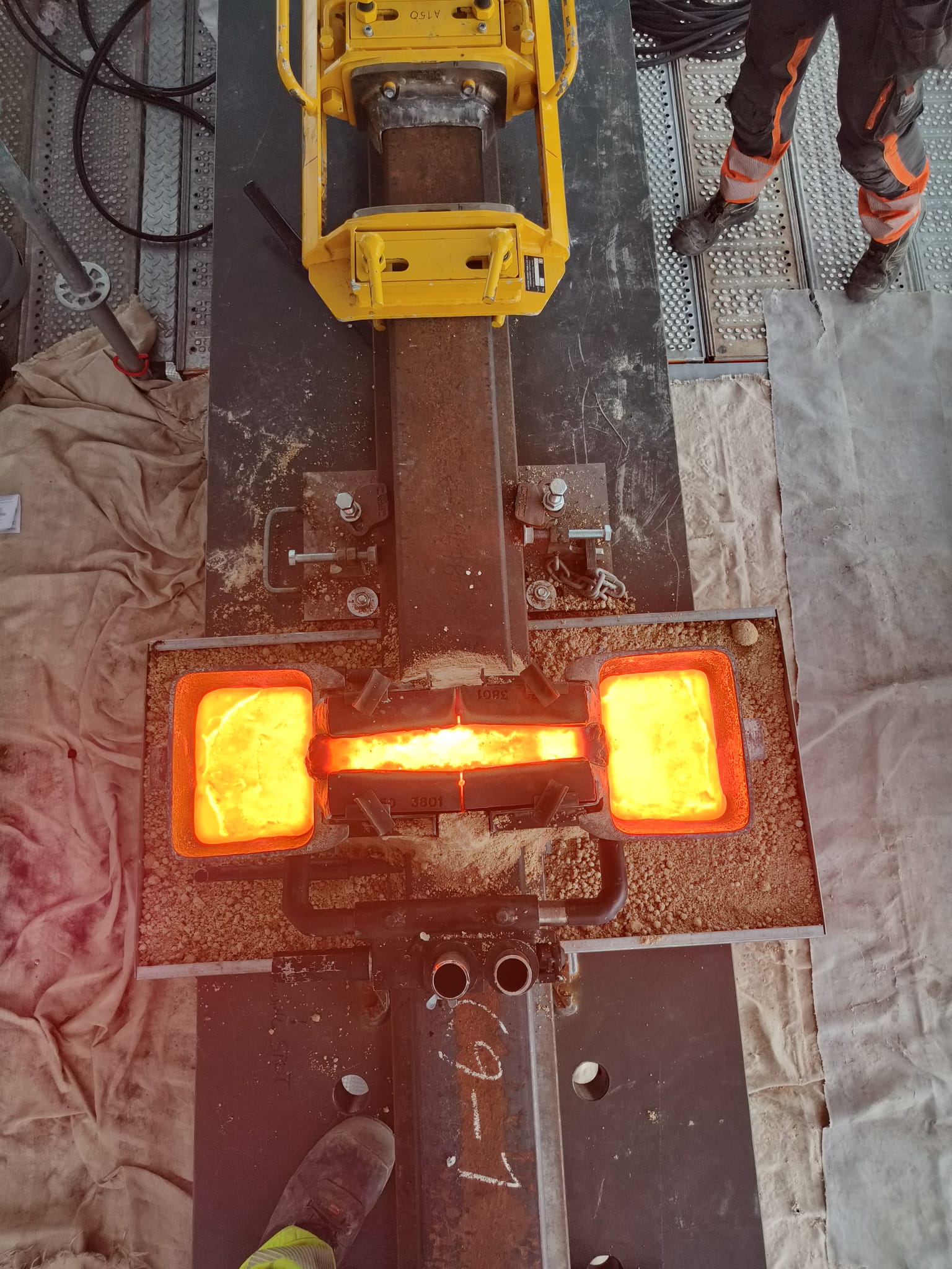 Rautatiekiskon alumiiniterminen hitsaus käynnissä. Sula metalli hohtaa kuumana kiskoliitoksen muotissa.